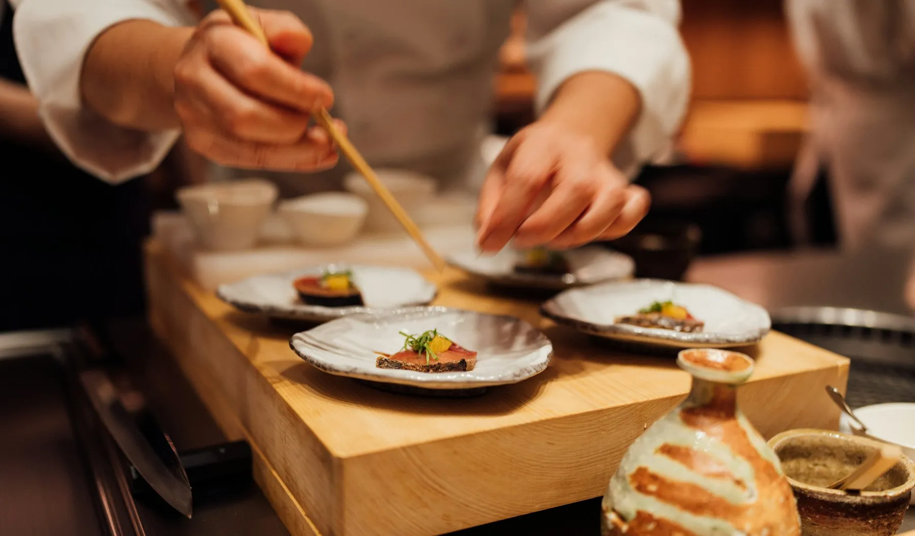 Koch richtet Sushi mit Stäbchen auf kleinen Tellern an